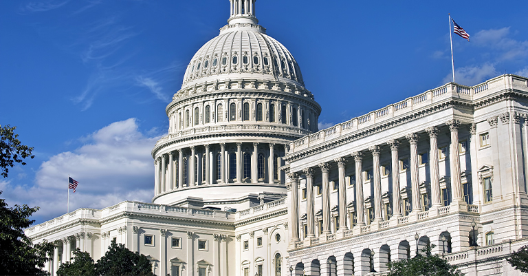 The United States Capitol building with its iconic dome and an American flag waving, under a clear blue sky.