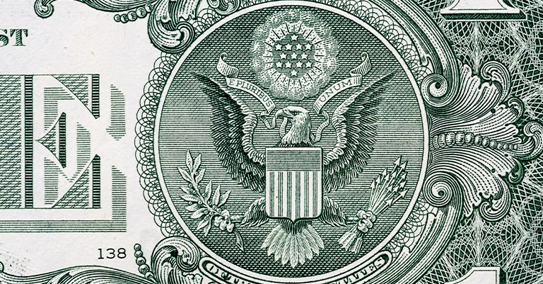 Close-up of the Great Seal of the United States on the back of a one-dollar bill, showing the bald eagle, shield, and Latin motto "E Pluribus Unum."