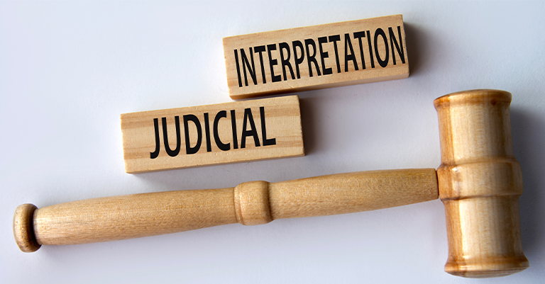 A wooden gavel next to two blocks labeled "JUDICIAL" and "INTERPRETATION" on a white background.