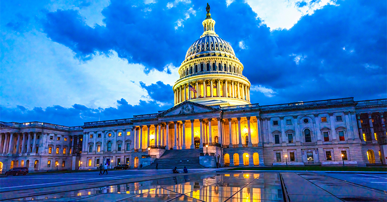 The U.S. Capitol building illuminated at dusk, reflecting on the ground, symbolizing democracy and legislative governance.